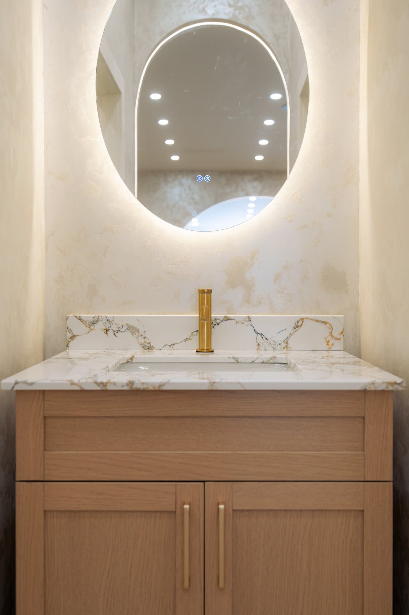Backlit oval mirror above the marble vanity