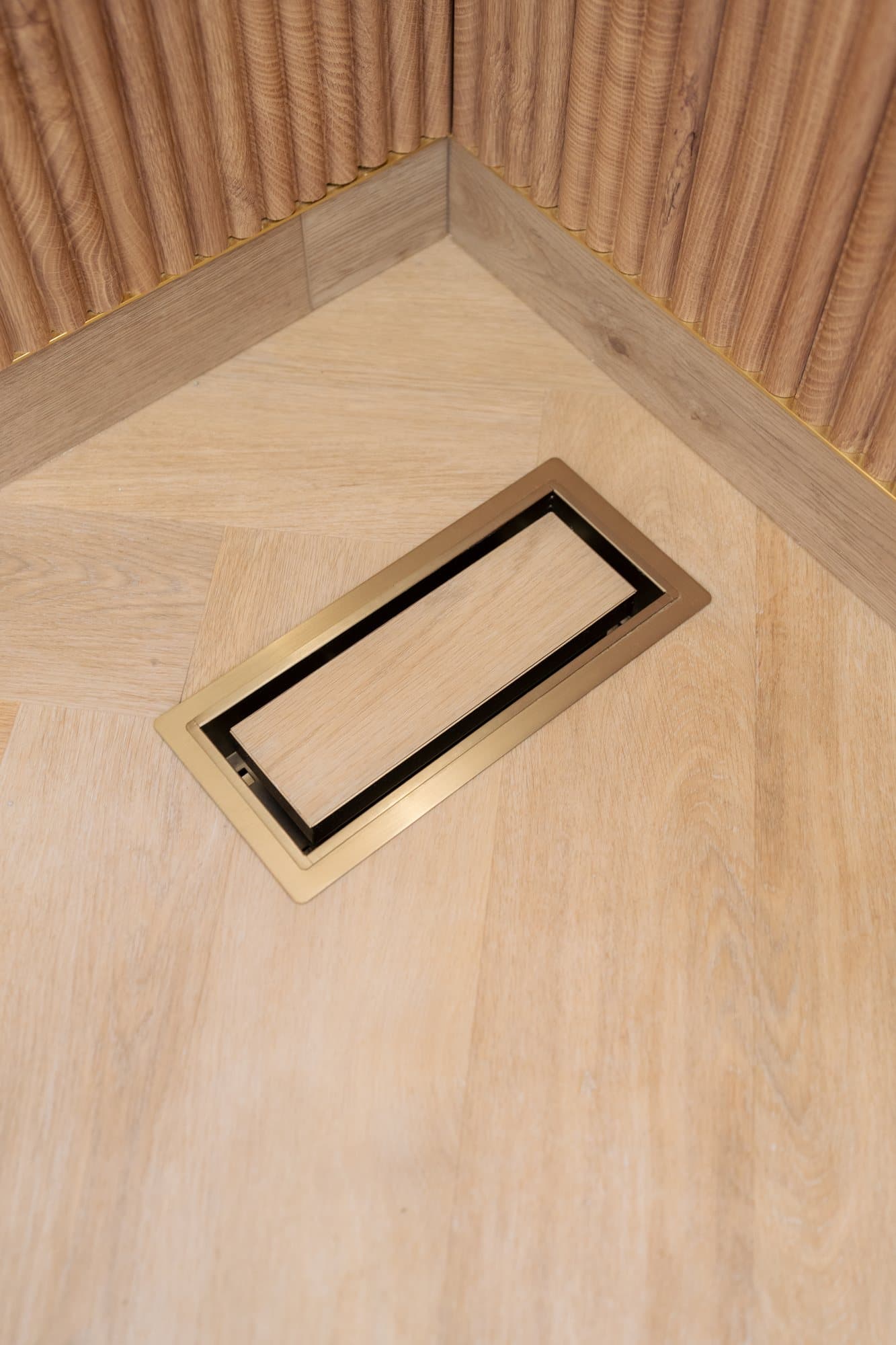 A brass-trimmed floor outlet inlaid into the herringbone
