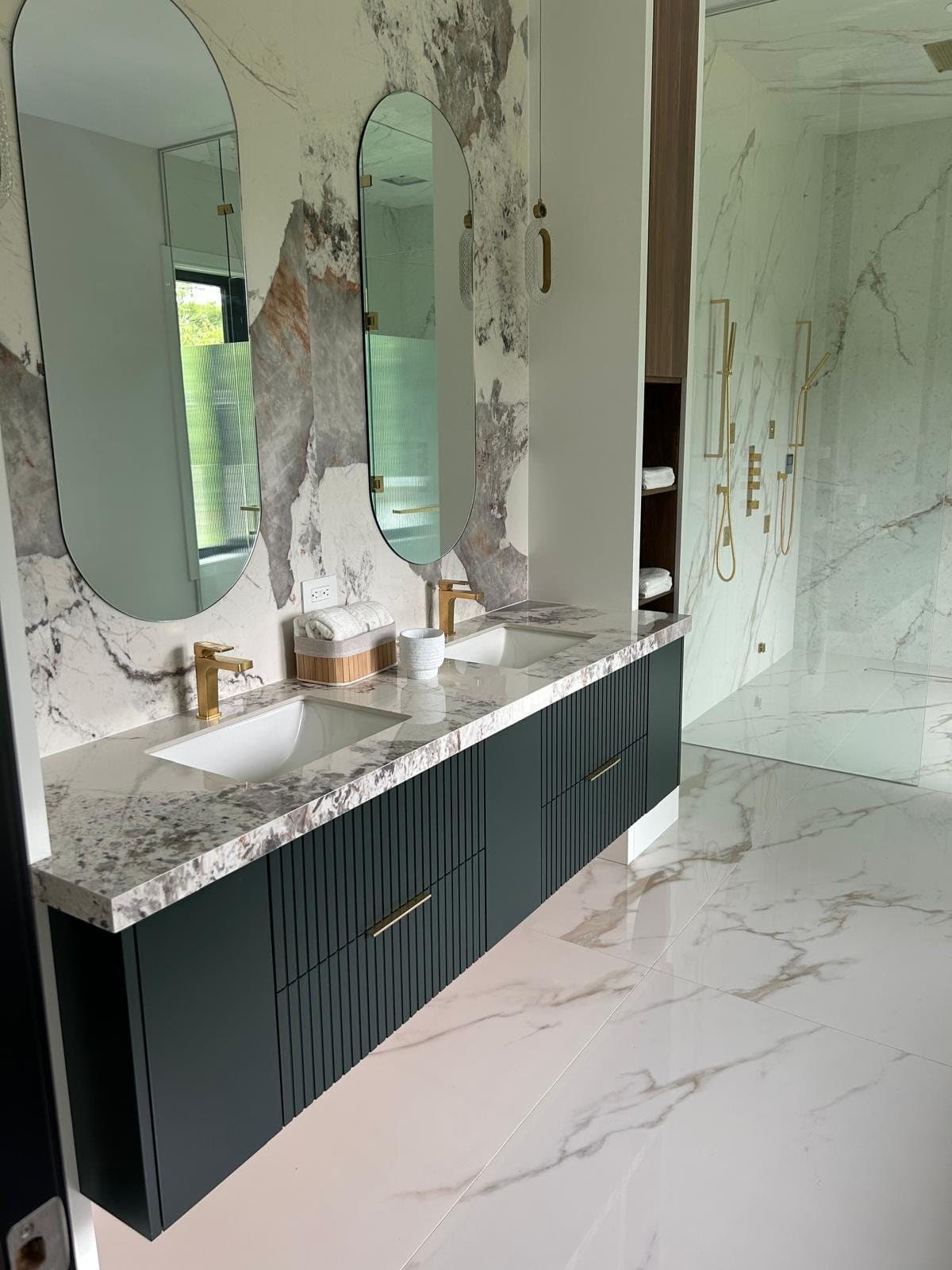 Charcoal fluted double vanity under two arched mirrors with a marble slab surround