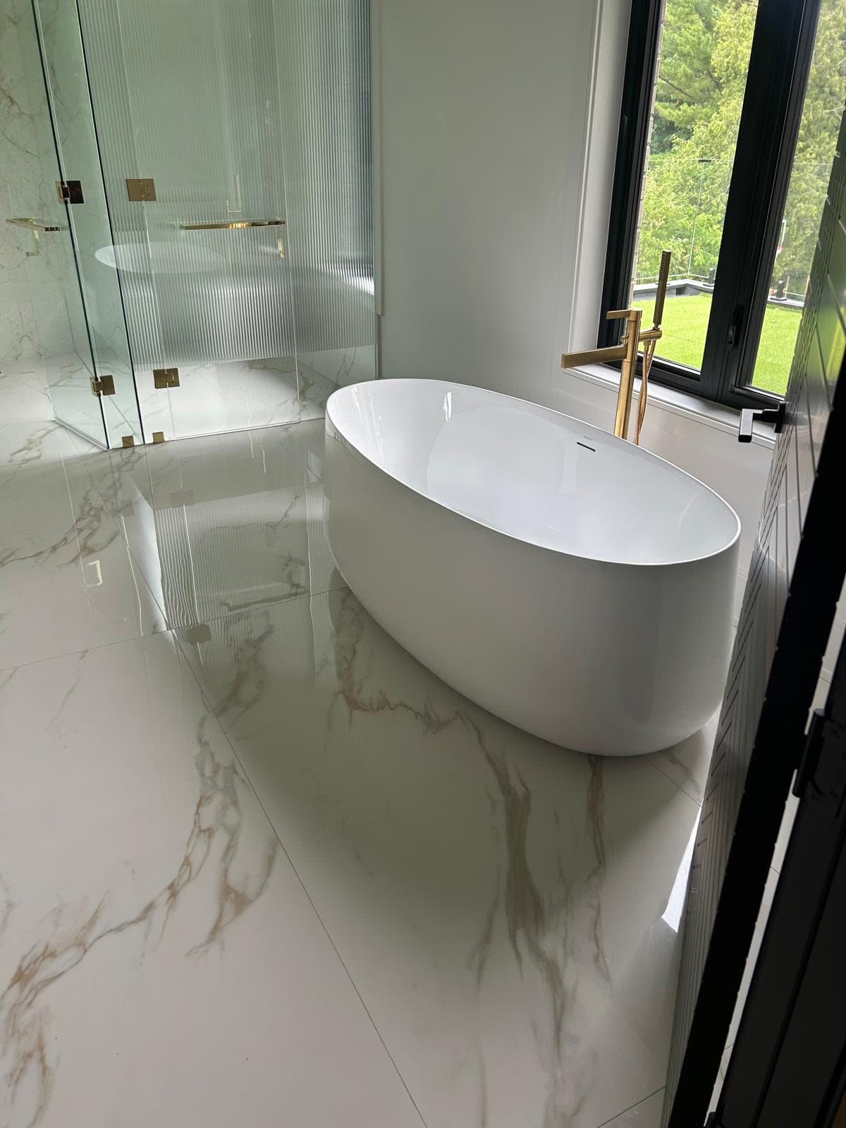 Freestanding tub against a marble slab wall with a floor-mounted brass filler