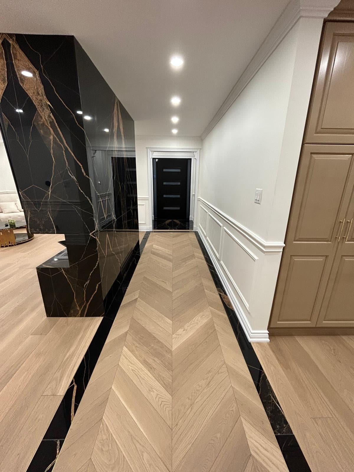 Hallway where a black marble slab border frames a chevron oak floor