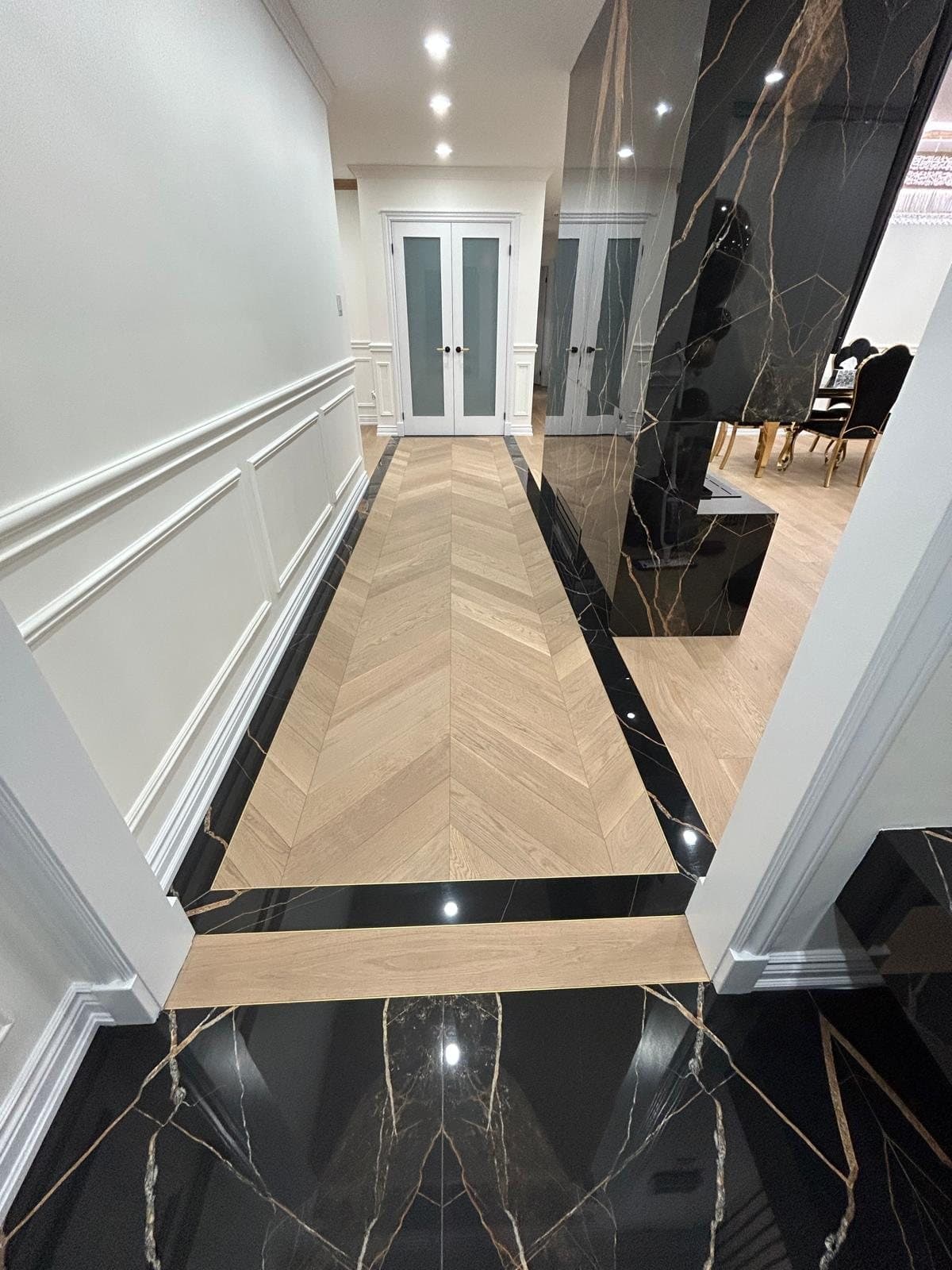 Hallway with a polished black marble border inlaid around chevron oak