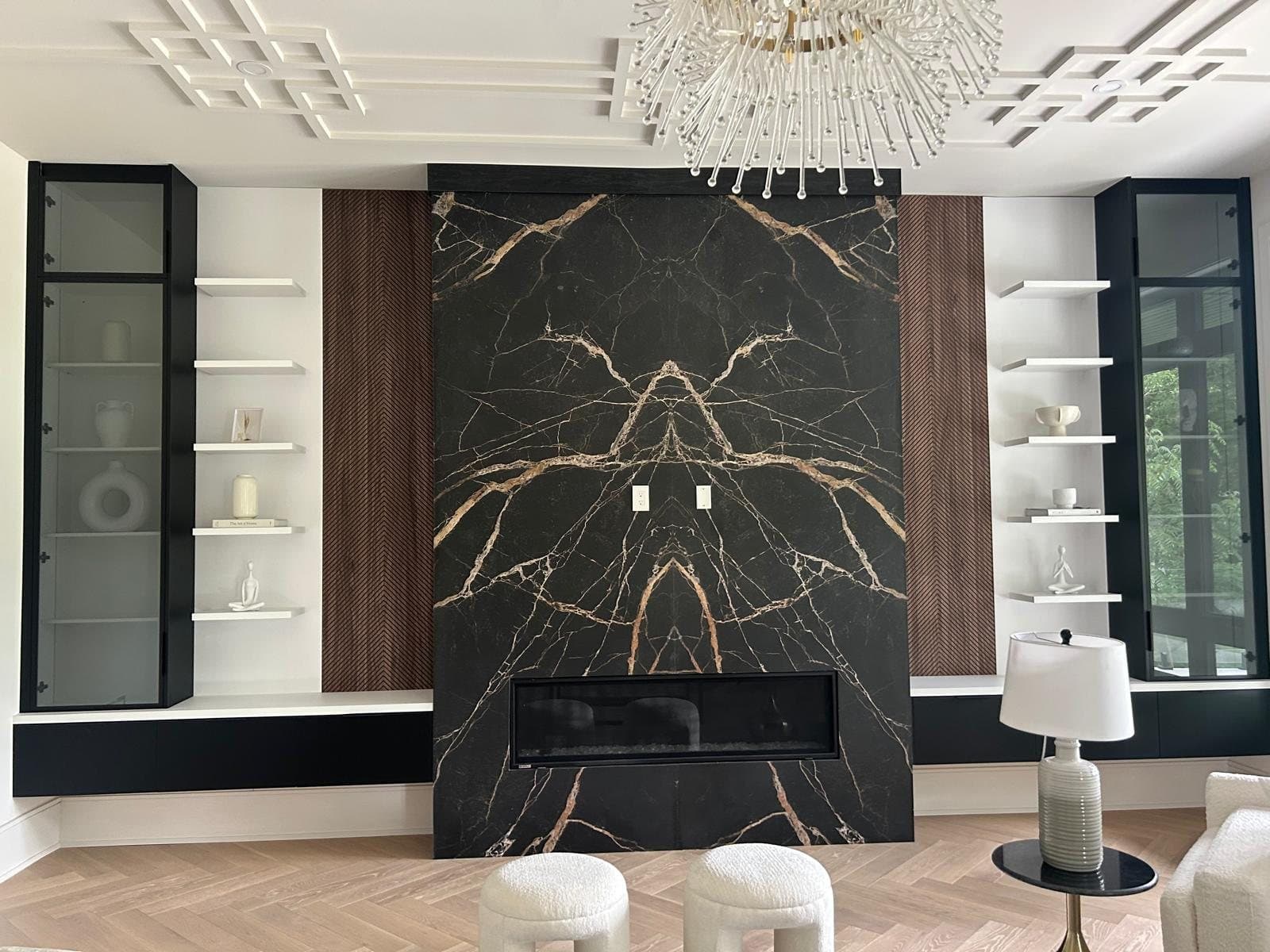 Living room with a book-matched noir marble fireplace, glass display cabinetry, and herringbone oak floor