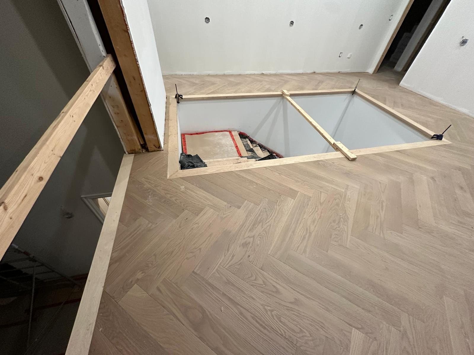 A stair opening cut and braced through a finished herringbone floor