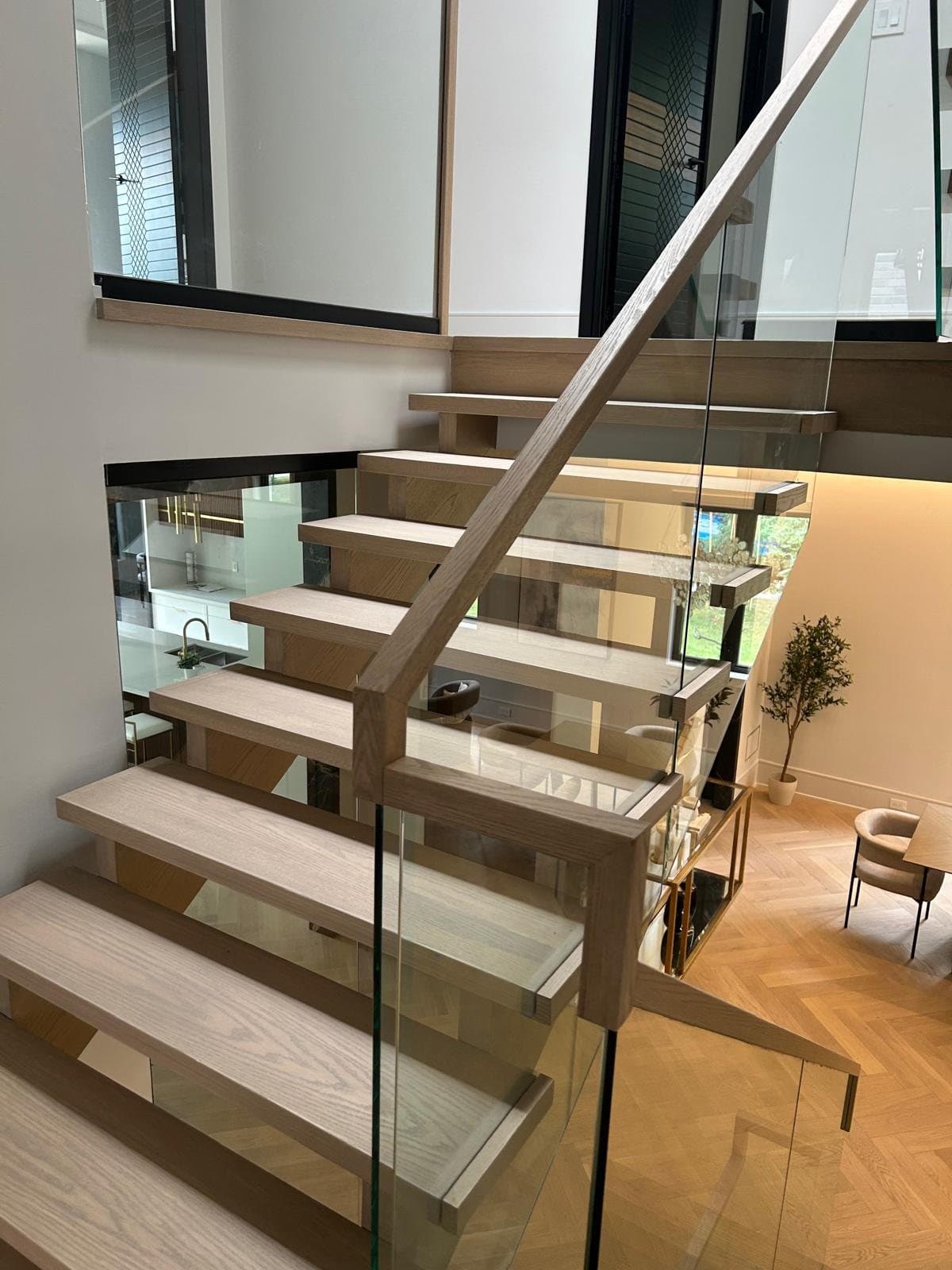 The finished open-riser white oak staircase with a frameless glass balustrade